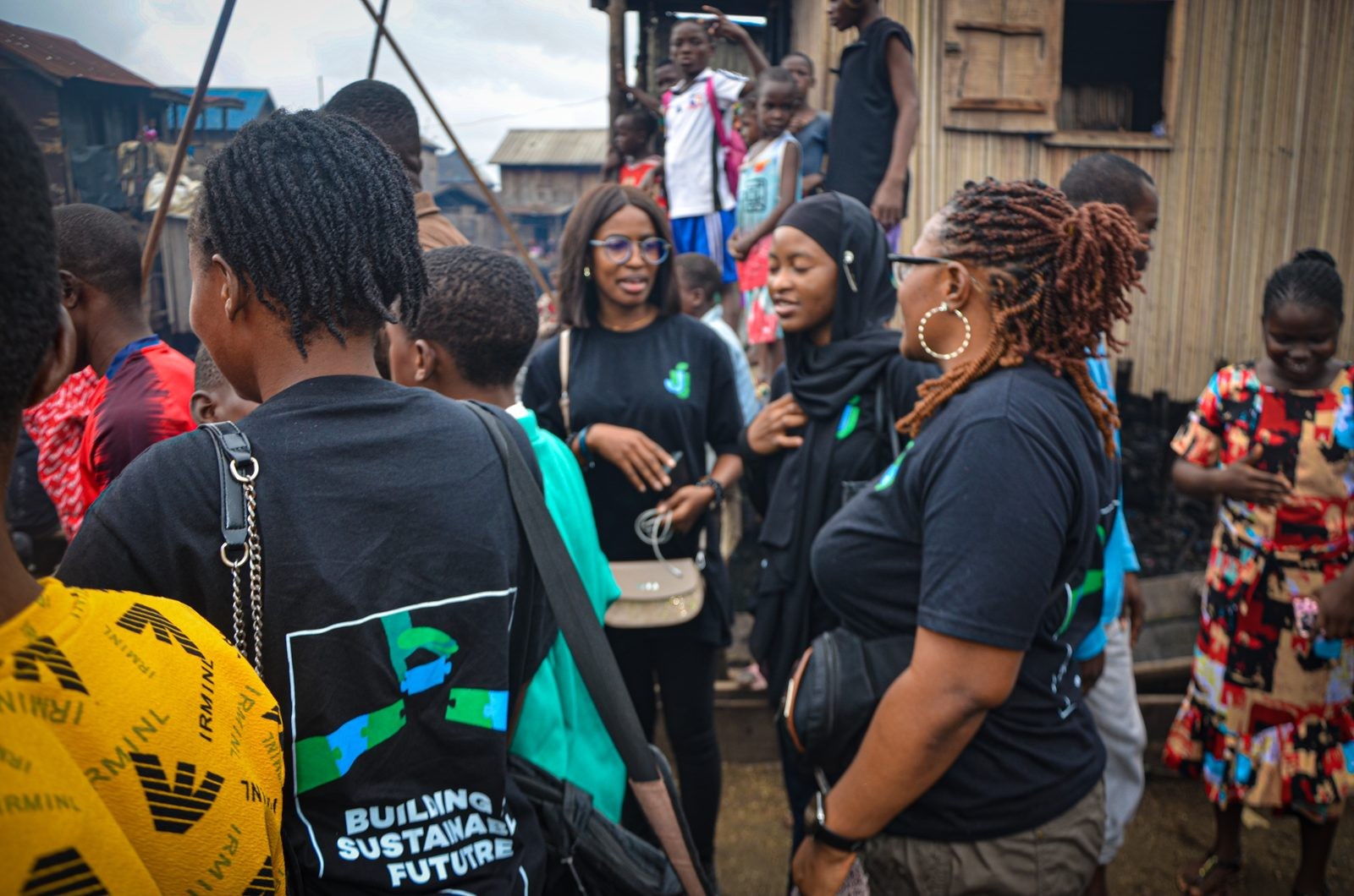 Team members in JustUsedTech shirts talking with residents in a Lagos waterfront community. (Lagos, since 2017)