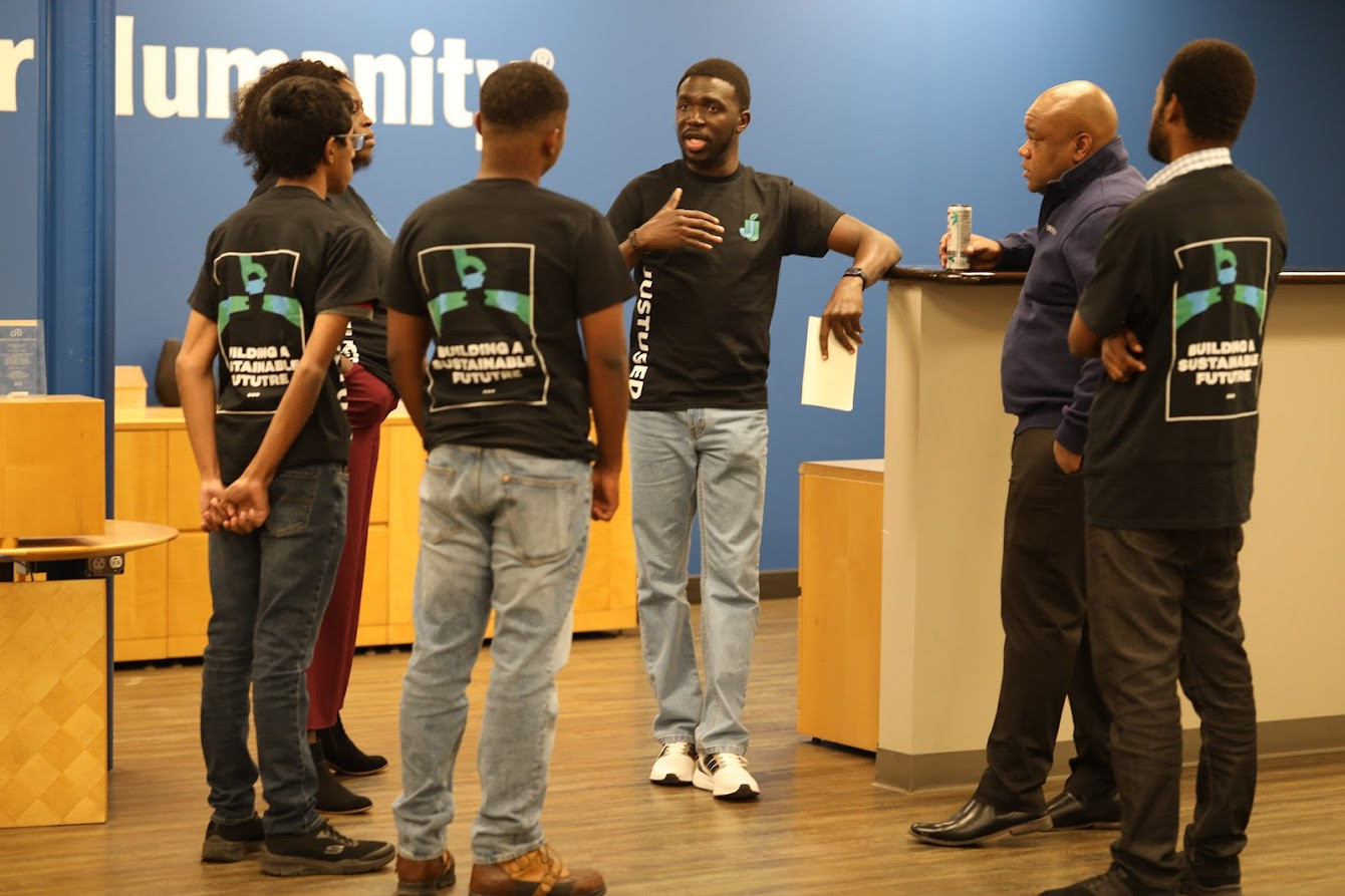 Team members in JustUsedTech shirts talking with visitors at an indoor event.