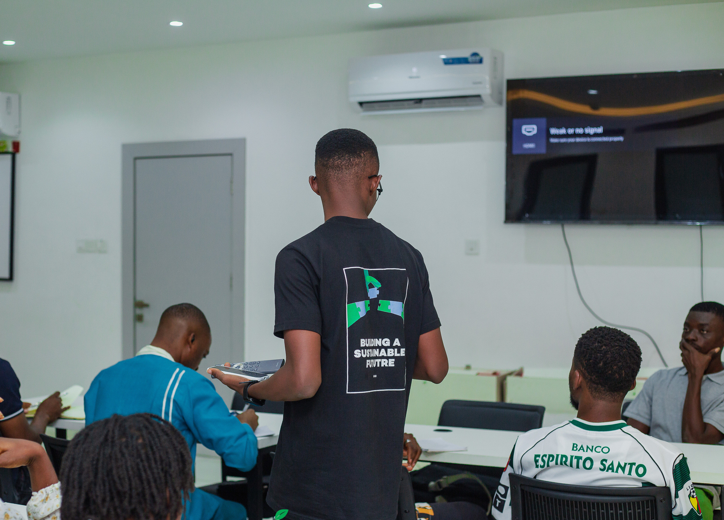 A facilitator in a JustUsedTech shirt standing at the front of a training room, with participants seated at desks.