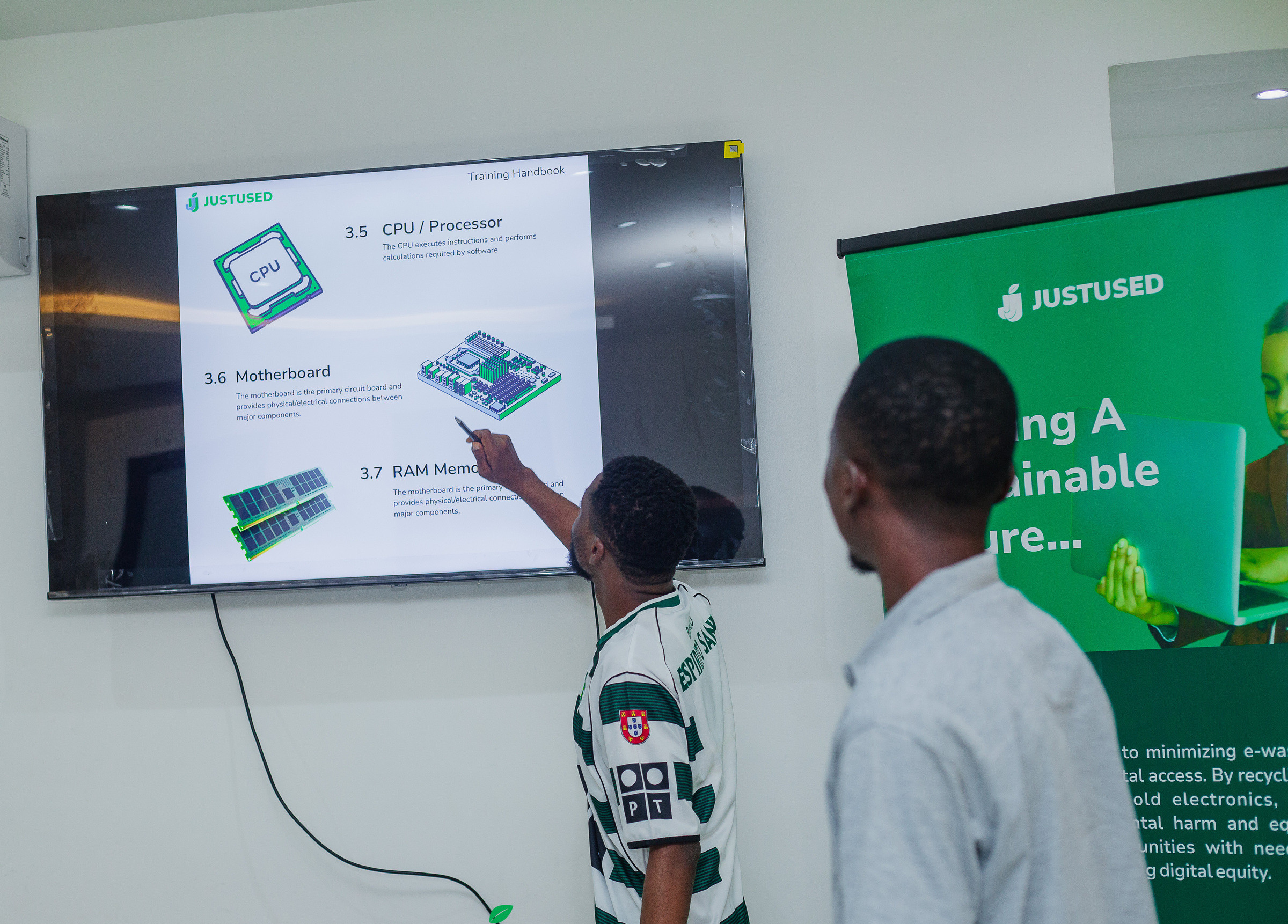 A facilitator pointing at a screen showing slides on CPUs, motherboards, and RAM, with a JustUsedTech banner beside it.