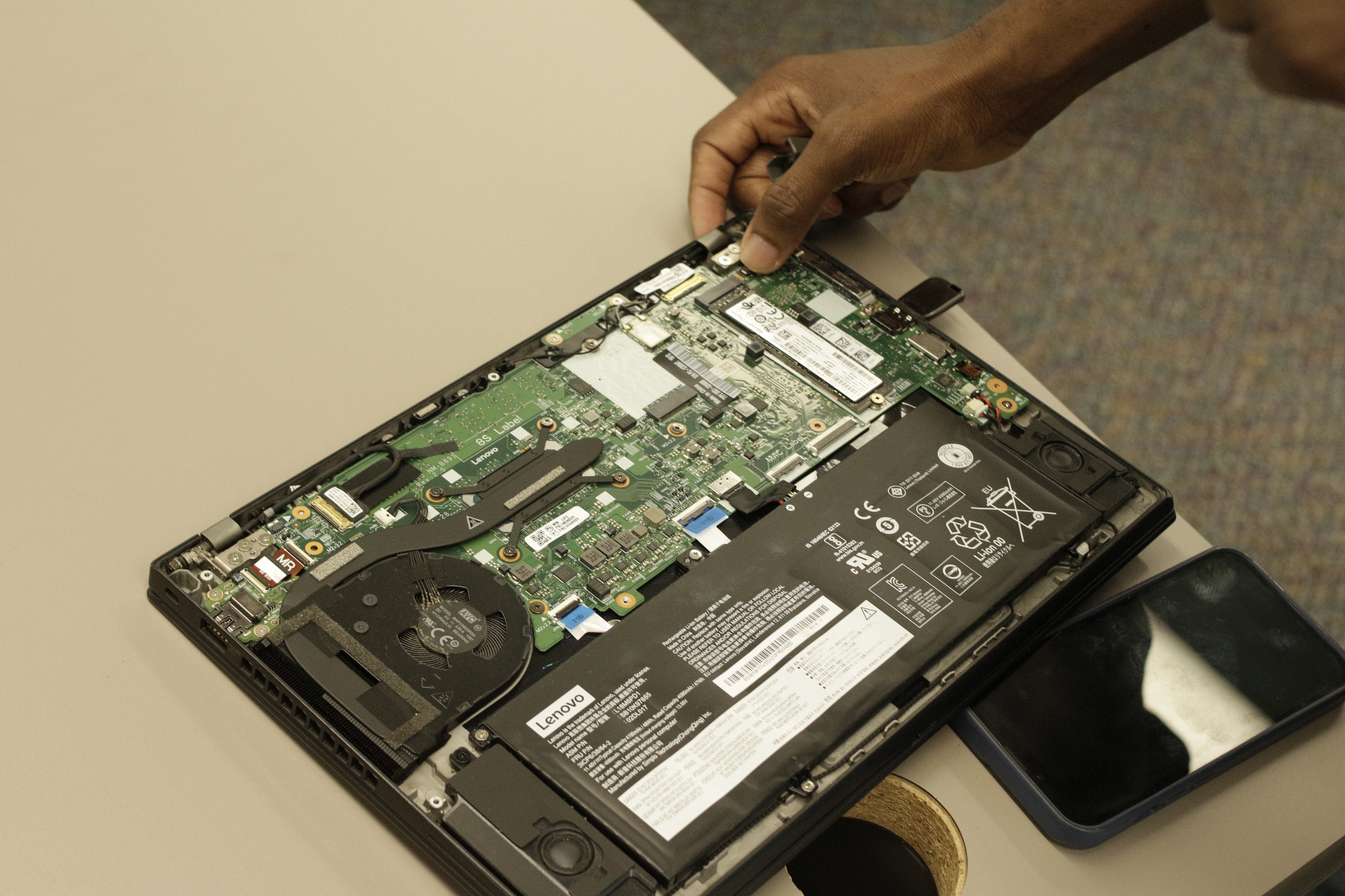 Close-up of an opened laptop with its back panel removed, a hand working on the internals.