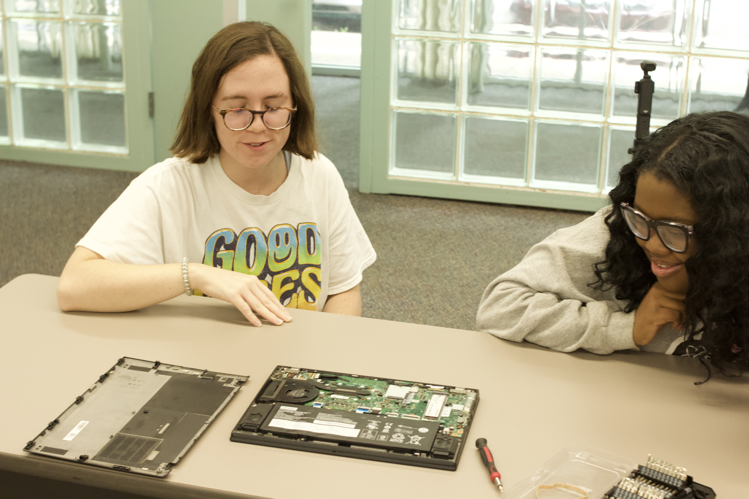 Two participants seated at a table behind a laptop that has been opened up, its back panel laid beside it.