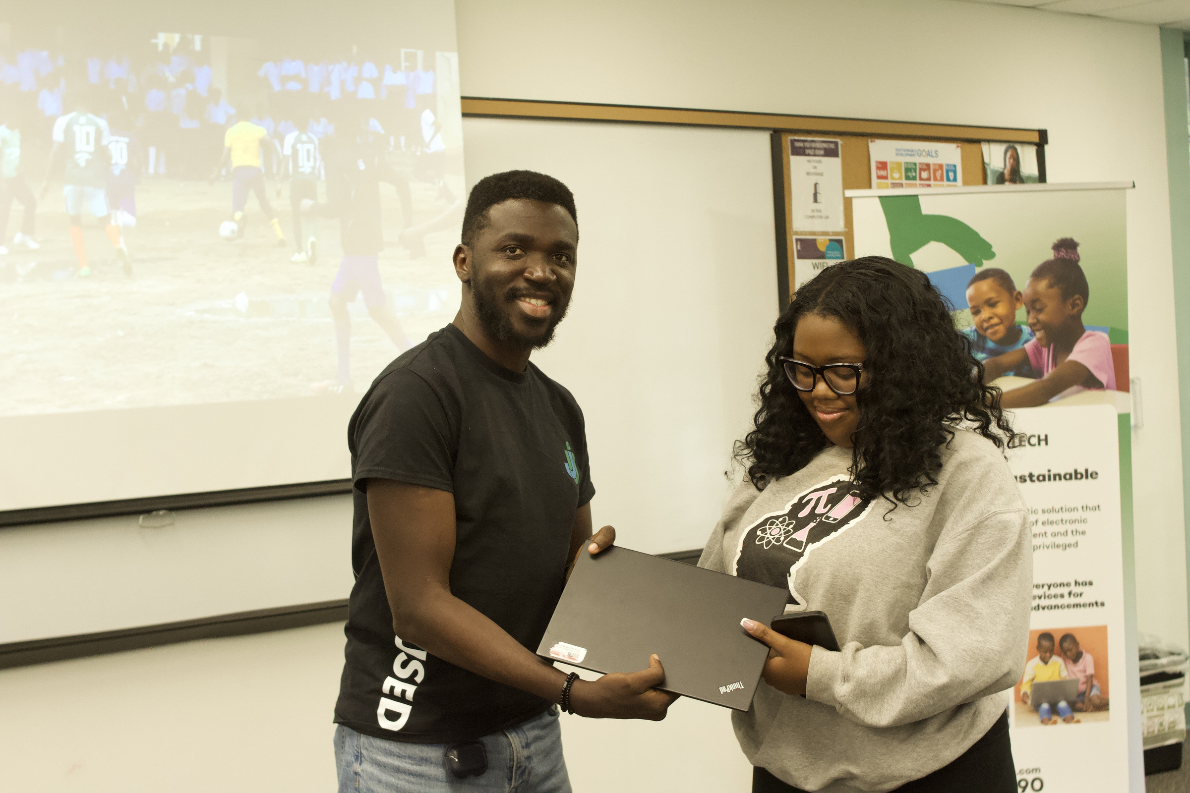 A team member in a JustUsedTech shirt handing a laptop to a participant in front of a JustUsedTech banner.