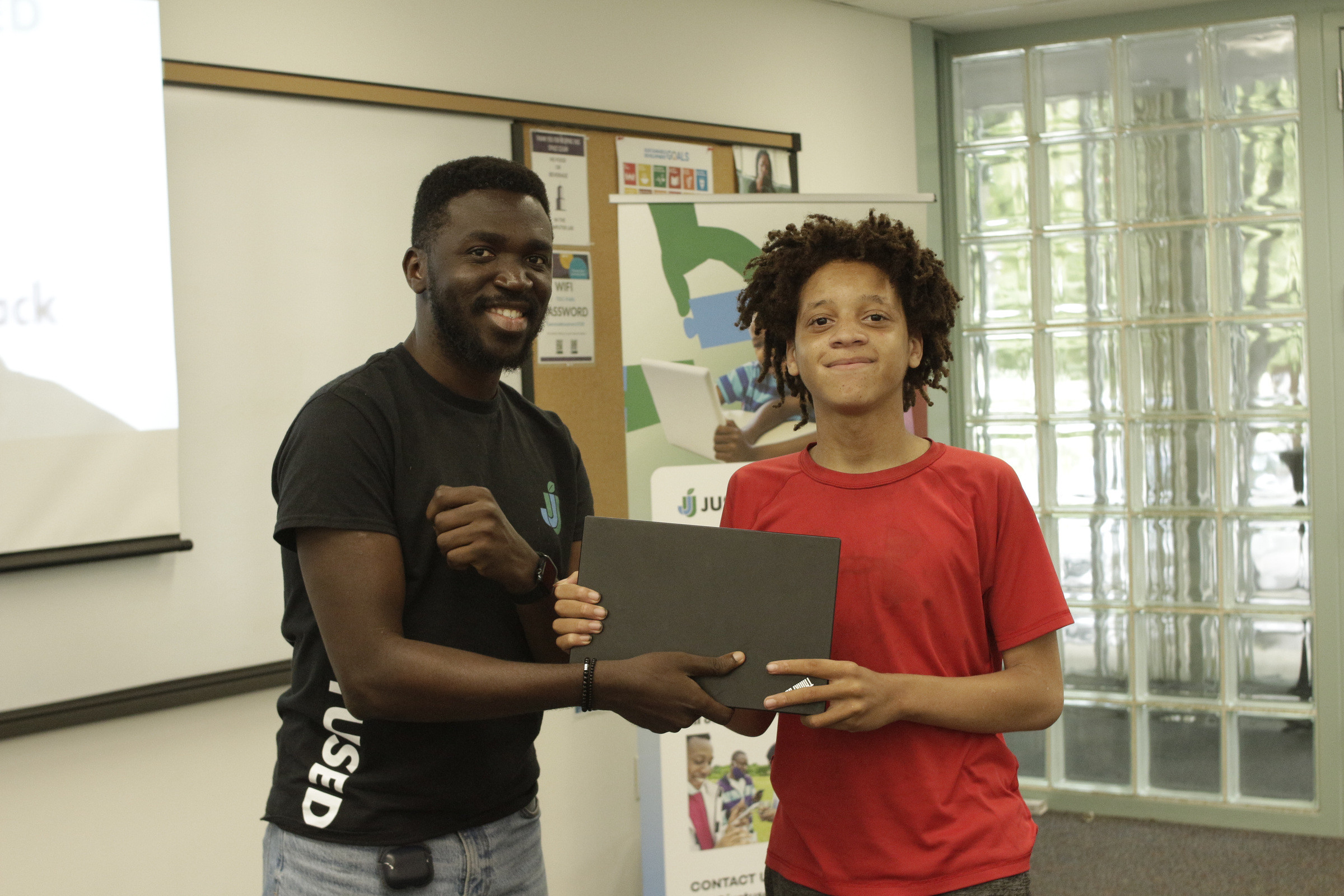A team member handing a laptop to a young participant in a red shirt.