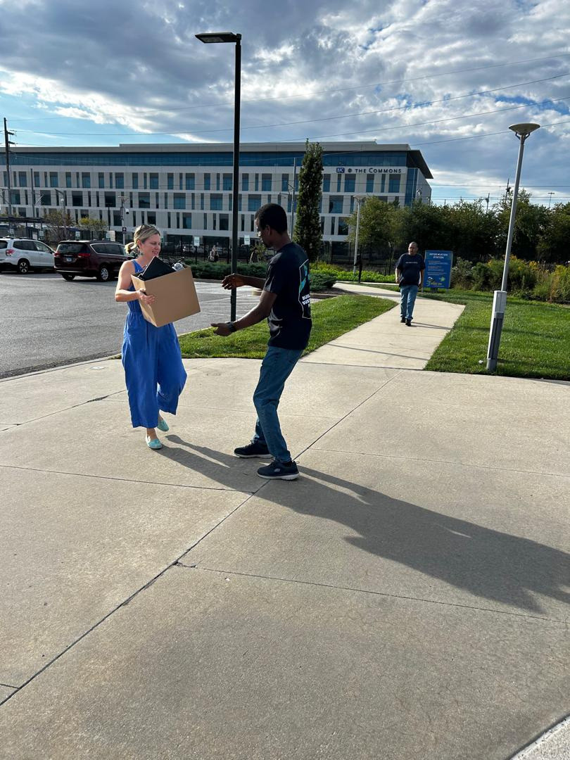 Two people carrying boxes across a plaza towards a collection point.