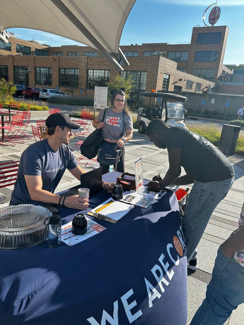 People working at a collection table under a canopy at an outdoor event.