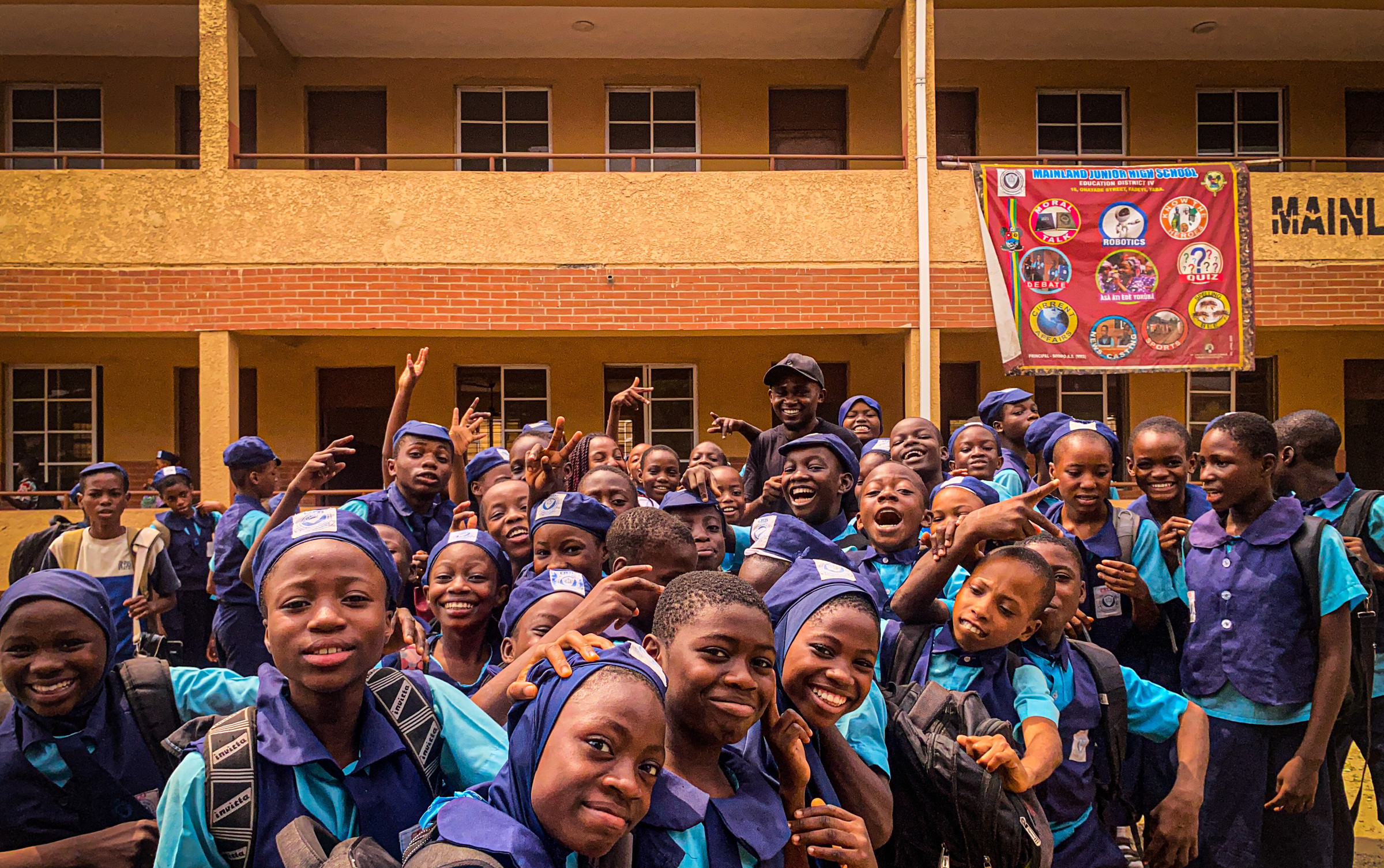 A large group of students in purple and blue school uniforms crowded together outside a school building, smiling towards the camera.