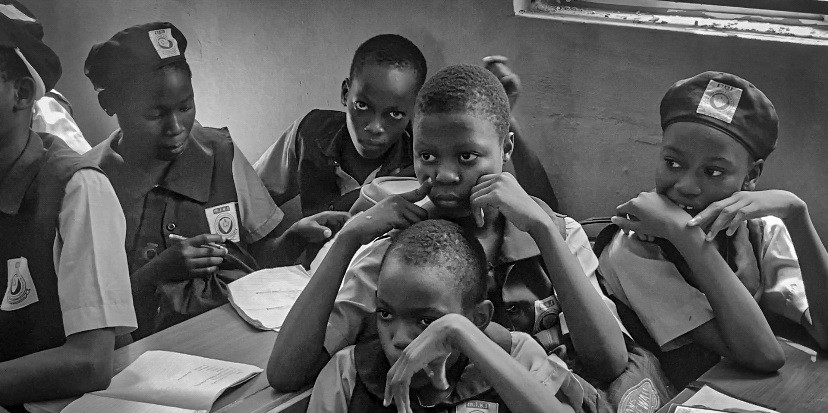 Black and white photograph of students at classroom desks leaning over open exercise books.