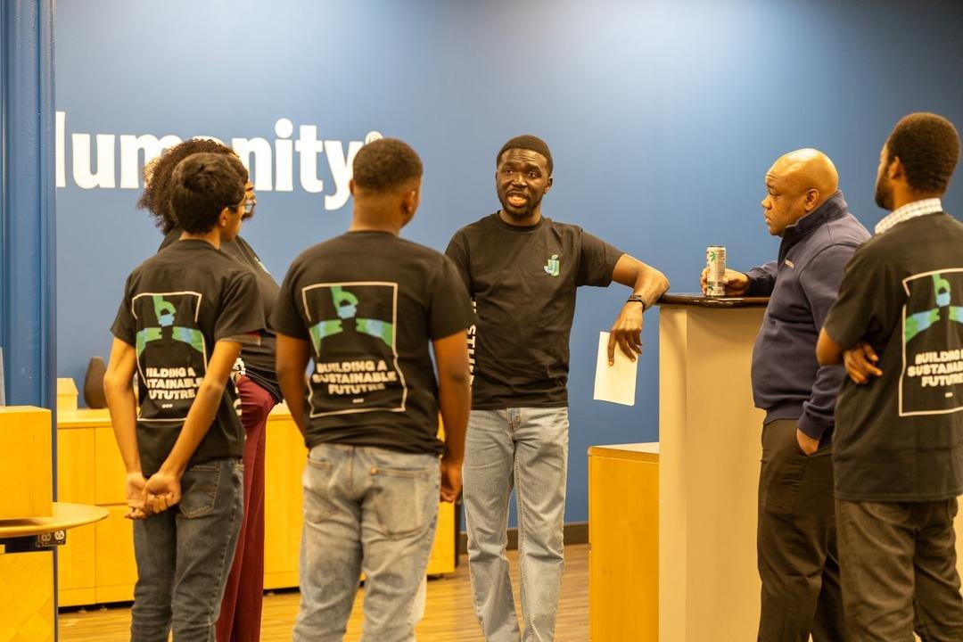 Five people, most in JustUsedTech shirts, standing in conversation around a high table in a community space.